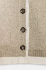 Chaqueta tipo cárdigan de lana en color beige, con diseño de tejido combinado que incluye una capa interior de tela clara. Presenta escote en pico, manga larga y cierre frontal con botones oscuros.