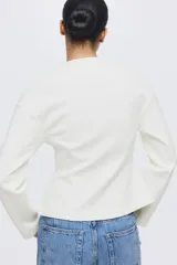 Blazer de botonadura sencilla en tejido efecto neopreno color blanco. Modelo de hombros caídos con escote redondo, botones hasta la cintura y corte acampanado de cintura a bajo.
