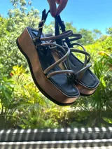 Sandalias marrones de plataforma con tiras finas cruzadas y hebilla ajustable en el tobillo.