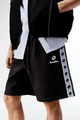 Short de felpa de mezcla de algodón en color negro, con corte regular fit, cintura elástica con cordón de ajuste y bolsillos laterales. Presenta franjas laterales blancas con el logotipo de la marca repetido y el logo de Lotto bordado en la pierna izquierda.