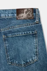Jeans wide leg de tiro bajo, confeccionados en denim con efecto lavado. Presentan diseño clásico de cinco bolsillos, cintura con trabillas y cierre frontal con cremallera y botón metálico.