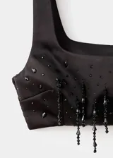 Top crop de satén negro con tirantes anchos, escote cuadrado y detalle de abalorios colgantes con pedrería en el bajo. Cuenta con panel elástico en la parte posterior.
