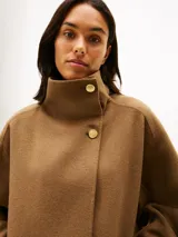 Abrigo de corte oversize confeccionado en mezcla de lana de doble cara, color marrón. Presenta cuello chimenea, cierre frontal con un botón visible y otro oculto, y dos bolsillos delanteros de parche.
