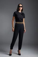 Remera negra de manga corta con aplique de flor en el hombro y cinturón de cadena dorada.