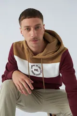 Buzo canguro de felpa color borgoña, con capucha ajustable con cordones color beige, bolsillo tipo canguro y logo estampado en el pecho. Tiene una franja horizontal blanca en el pecho y puños y cintura acanalados.