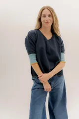 Buzo de punto con escote en V y mangas 3/4. Presenta un diseño de color gris oscuro con puños acanalados en tono celeste y detalles en amarillo en los bordes. Posee un corte holgado con tajos laterales.