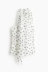 Top entallado en malla transparente, de color blanco con estampado de lunares negros. Presenta escote asimétrico, un solo hombro y tiras anchas para anudar al cuello.