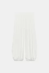 Pantalón de tiro medio confeccionado en tejido satinado blanco, con cintura elástica, diseño plisado y bajo abullonado y asimétrico.