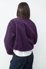 Campera bomber corta de pana color violeta, con cierre frontal de cremallera, cuello redondo y mangas largas con puños elásticos.