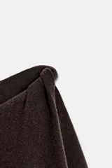 Jersey de punto color marrón oscuro, con cuello redondo y manga larga. Presenta un diseño con aberturas y nudos decorativos en los hombros.