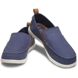 Mocasín Crocs modelo Walu Syn de estilo náutico, confeccionado en lona azul con detalles en color marrón. Presenta suela de material Croslite flexible y diseño slip-on con ojales decorativos laterales.