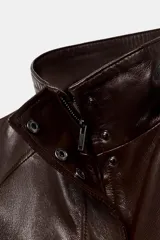 Chaqueta bomber de piel color marrón oscuro, con cuello alto, cierre frontal con cremallera y solapa con botones ocultos. Presenta mangas largas, bolsillos delanteros y un diseño de corte recto.