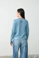 Remera de punto color celeste con cuello polo, manga larga y detalles de rayas en contraste en cuello, puños y ruedo.