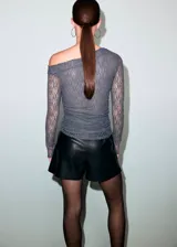 Top de encaje gris oscuro con diseño semitransparente, cuello asimétrico de hombro descubierto y manga larga.