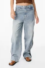 Jean de corte recto y tiro medio, confeccionado en denim de algodón en tono azul claro. Presenta un diseño distintivo con cierres laterales a lo largo de las piernas y detalles de costuras desflecadas.