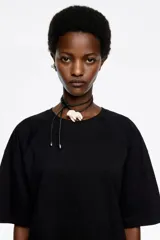 Camiseta negra de corte recto y largo medio, confeccionada en algodón orgánico. Presenta escote redondo, mangas cortas amplias con costuras raglán y detalles de cortes diagonales en el cuerpo.