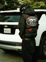 Chaleco puffer negro con capucha, estampado de manos rojas y logo bordado. Cuenta con cierre frontal y bolsillos con cierre.