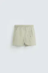 Bañador de hombre color verde claro con finas rayas blancas verticales (efecto seersucker). Tiene cintura elástica ajustable con cordón verde, bolsillos laterales y un bolsillo trasero de vivo.
