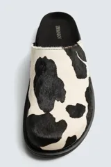 Zueco de piel con pelo con estampado de vaca en blanco y negro. Presenta una horma redonda y una suela de goma negra con volumen.