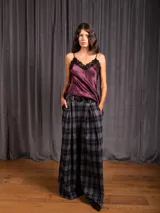 Pantalón tipo palazzo de corte amplio y tiro alto, con diseño de estampado a cuadros tipo tartán en tonos grises y negros. Presenta pinzas frontales, bolsillos laterales y cierre con trabillas para cinturón.