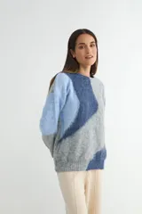 Buzo de tejido de punto con diseño de bloques de color en tonos blanco y gris, de cuello redondo y manga larga.