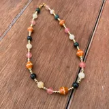 Collar corto elaborado con cuentas de piedras naturales facetadas en tonos naranjas, rosas, verdes y cremas, intercaladas con pequeñas cuentas doradas.