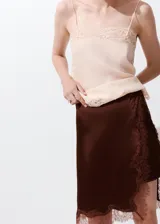 Falda midi recta de satén color marrón, con tiro regular y detalle de puntilla en el ruedo y el lateral.