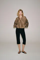 Camisa fluida de Zara Woman Collection, confeccionada en hilatura con mezcla de viscosa en tono tostado. Presenta cuello redondo, mangas largas con puños elásticos y diseño fruncido en la parte delantera. Dispone de cierre frontal con botones ocultos por solapa.