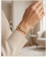 Pulsera de plata 925 con baño de oro, compuesta por una cadena de malla metálica y dijes decorativos, incluyendo una mariposa central con incrustaciones de circonias.