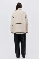 Campera de corte holgado confeccionada en tejido de sherpa suave, con cuello alto y cierre frontal. Presenta detalles de ribetes en contraste y diseño de hombros caídos.