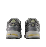 Championes urbanos New Balance modelo 1906R, color gris con detalles en amarillo. Presentan una estructura técnica con paneles de malla y refuerzos sintéticos, entresuela con tecnología de amortiguación y logo N lateral.