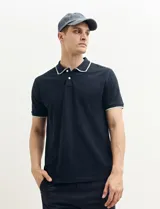 Remera polo azul marino con ribetes blancos en el cuello y en los bordes de las mangas corta, y cierre frontal de botones.