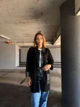 Camisa larga negra con cuello clásico, cierre frontal con botones a presión, mangas largas con puños de cuero y bolsillos de cuero con pespuntes blancos.