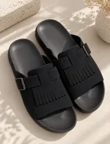 Sandalia negra de diseño destalonado con capellada ancha, detalle de flecos y tira con hebilla ajustable metálica.