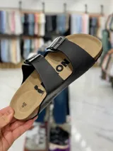 Sandalias de dos tiras negras con hebillas metálicas ajustables, plantilla anatómica y suela plana.