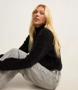 Suéter negro de punto con hilos metálicos, cuello alto y mangas largas.