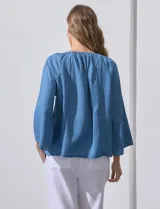 Blusa celeste de lyocell con cuello a la base y escote en V con lazo de ajuste. Manga larga amplia.