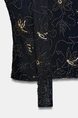 Top tipo corset o bandeau color marrón oscuro, con bordado de cuentas y lentejuelas blancas que forman patrones florales y asteriscos. Incluye un largo lazo/foulard a juego que funciona como tirante halter y se extiende hacia abajo.