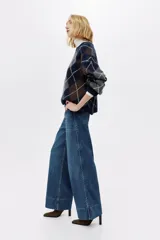 Jean de corte wide leg tiro alto, confeccionado en denim azul con efecto desgastado. Presenta diseño de cinco bolsillos, detalles trenzados a los lados y dobladillo ancho pespunteado.