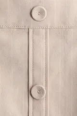 Short pollera de sarga color beige con diseño tableado, tira frontal con botones forrados decorativos y sutiles rayas finas.