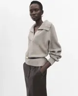 Jersey de punto color beige, con cuello polo, escote en V y mangas largas con puños ajustados. Presenta una textura acanalada y un diseño holgado.
