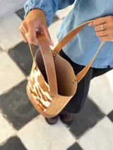 Bolso tipo matera confeccionado en cuero, con diseño combinado que presenta laterales con textura de cocodrilo y panel central con estampado animal print de vaca. Cuenta con asas largas para llevar al hombro y base reforzada.