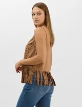 Blusa sin mangas de textura gamuzada color marrón, con escote redondo y corte recto. El frente presenta un diseño de calados circulares y geométricos, finalizando en un ruedo con flecos largos.