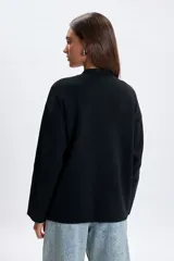 Campera de punto color negro con cierre frontal, cuello redondo y mangas largas. Presenta un diseño minimalista y versátil con cordones ajustables en la parte inferior.