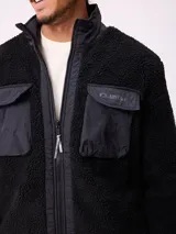 Campera reversible de sherpa y nylon, color negro, con cierre frontal, cuello alto y bolsillos frontales con solapa.