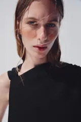 Vestido midi negro de cuello redondo y manga sisa, con detalle de drapeado en la cintura y cierre lateral con cremallera oculta.