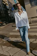 Camisa de cuello solapa y manga larga, con cierre frontal de botones y puños ajustables decorados con lazos del mismo tejido.