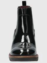 Bota tipo Chelsea de caña corta en charol negro, con paneles laterales elásticos, suela track robusta y taco cuadrado. Presenta un detalle de costura en color rojo en la base de la suela.