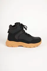 Zapatilla tipo bota de estilo hiking, confeccionada en una combinación de cuero sintético y nylon. Presenta un diseño en color negro con suela de goma dentada en tono caramelo, cordones al tono y cuello acolchado para mayor confort.