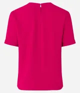 Blusa blanca de poliéster con cuello redondo, mangas cortas, cierre trasero en forma de gota, pequeñas aberturas laterales y acabados en pespuntes en las mangas y el cuello.